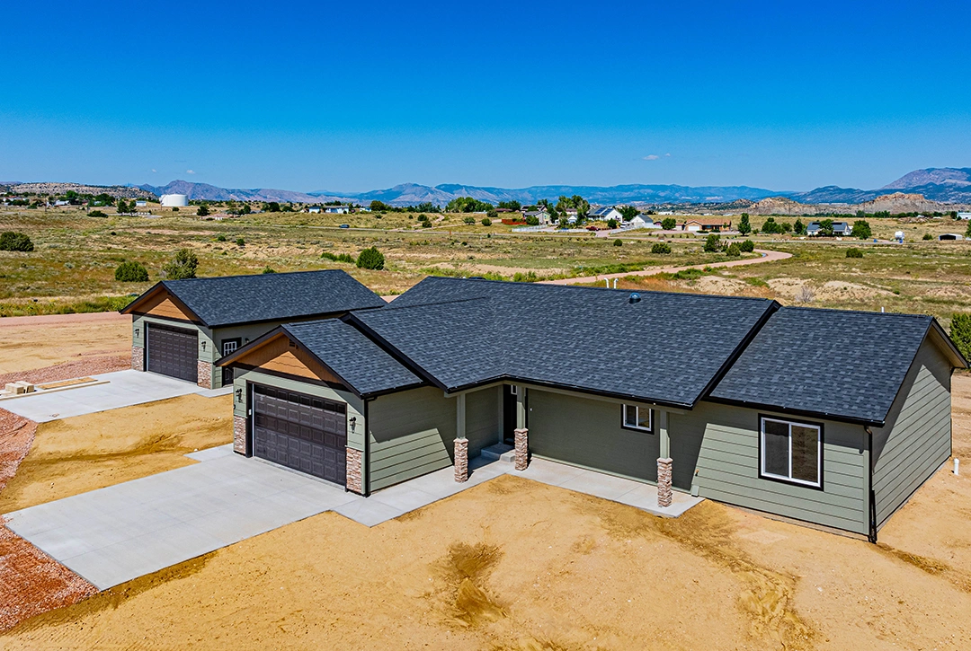 Custom ranch home built by Helton Construction on spacious Colorado lot, featuring green siding with black trim, attached two-car garage, and panoramic mountain views of the Wet Mountains